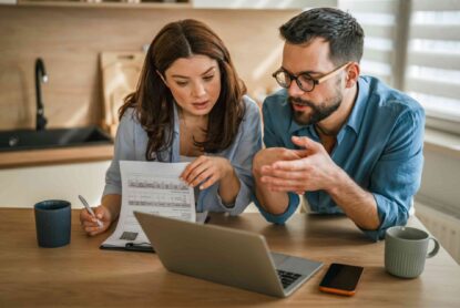 A couple at their kitchen table reading a letter from their bank beside a laptop, weighing whether to accept a retention offer or switch lenders.