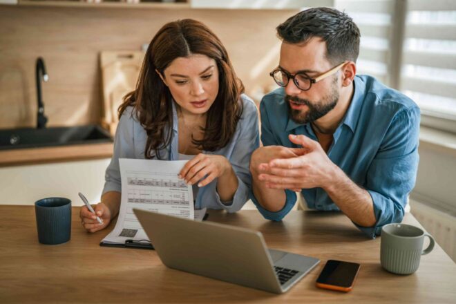 A couple at their kitchen table reading a letter from their bank beside a laptop, weighing whether to accept a retention offer or switch lenders.